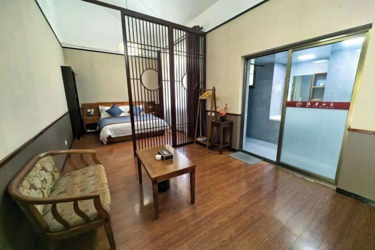 A room with a bed, a wooden table, a chair, and a sliding door leading to another room.