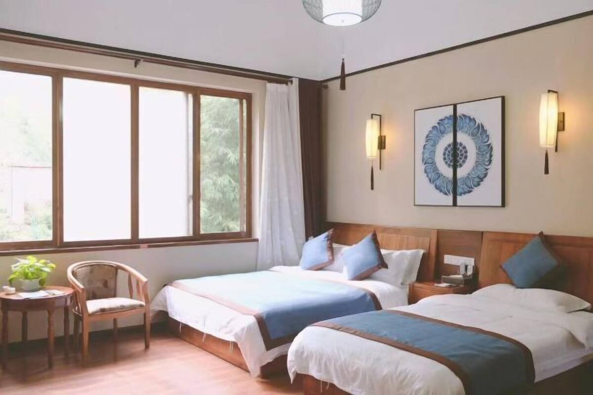 A hotel room with two beds, a chair, a small table, and a window with curtains.