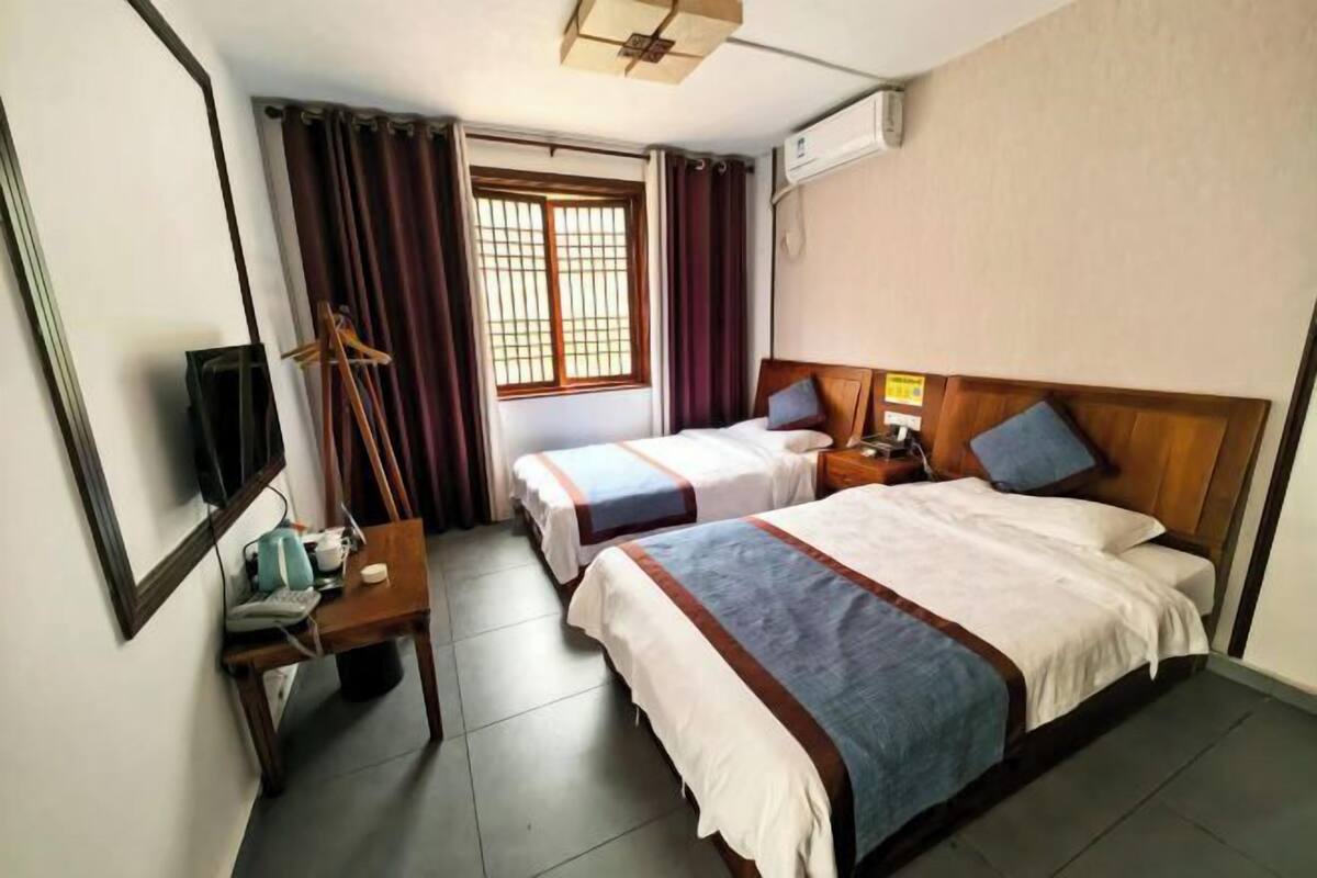 A hotel room with two beds, a desk with a chair, a TV, and a window with curtains.