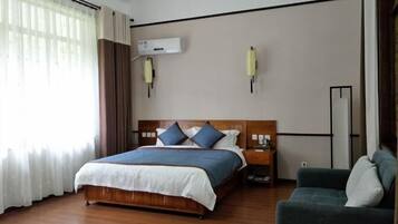 A hotel room with a wooden bed, a green armchair, a bedside table, and an air conditioning unit on the wall.