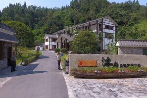 A traditional-style building with a tiled roof and wooden beams, surrounded by lush greenery and hills. - Mufu Leisure Mountian Resort (Muchuan)