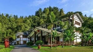 A two-story building with a central entrance, surrounded by lush greenery and palm trees. - Mufu Leisure Mountian Resort (Muchuan)