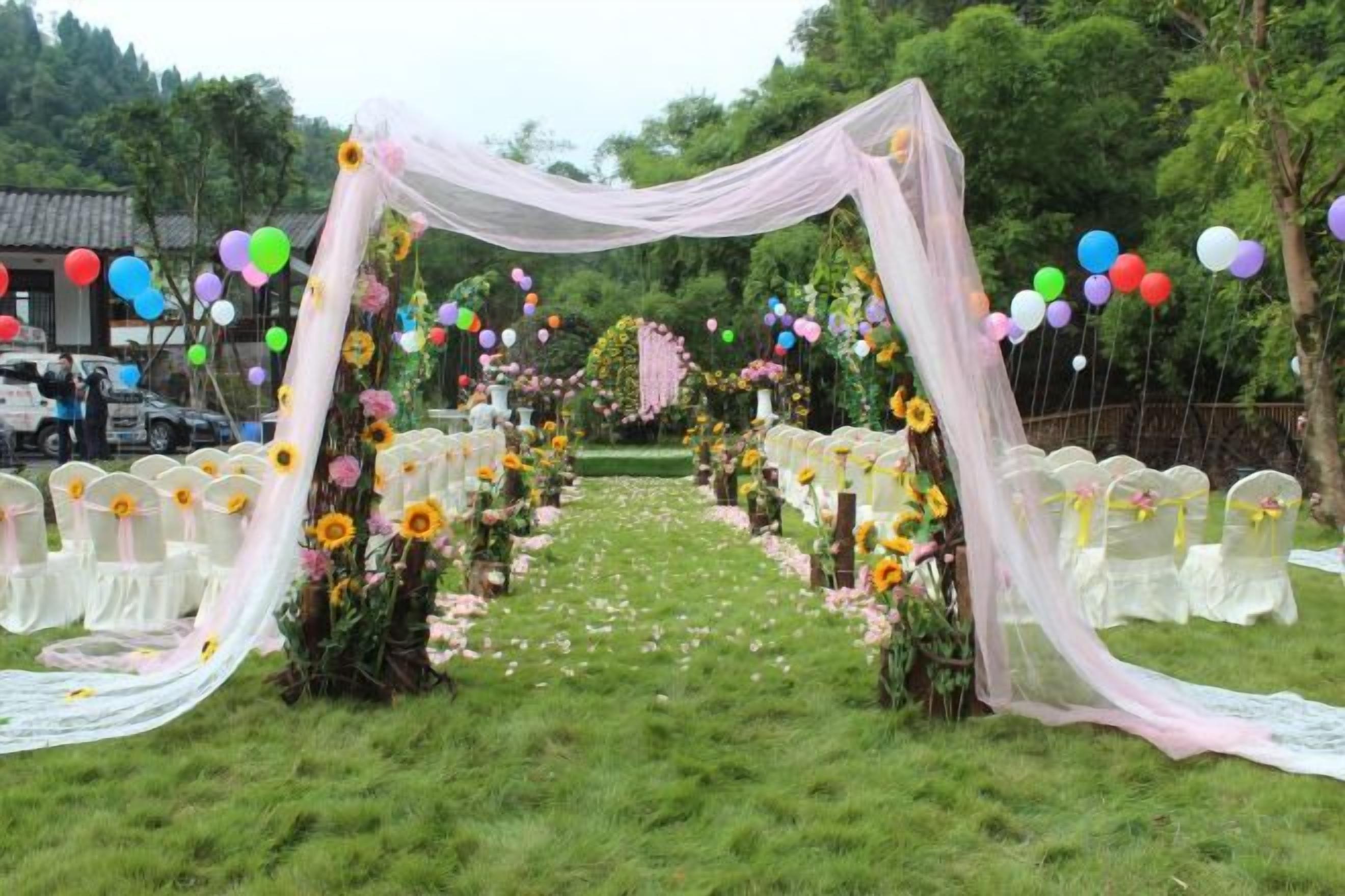 An outdoor wedding venue with a floral archway, white chairs, and a grassy aisle.