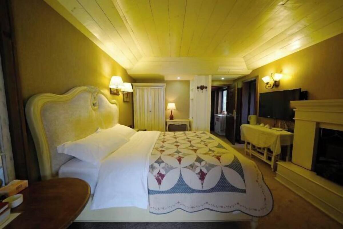 A hotel room with a bed, bedside lamps, a television, a fireplace, and a small table.