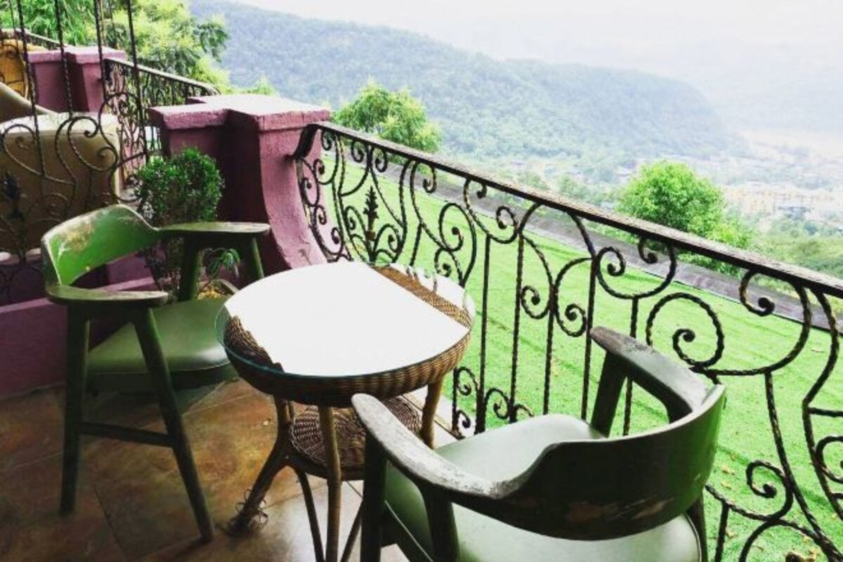Un balcon avec une table et des chaises, une rambarde en métal décorative et une vue sur un paysage verdoyant.