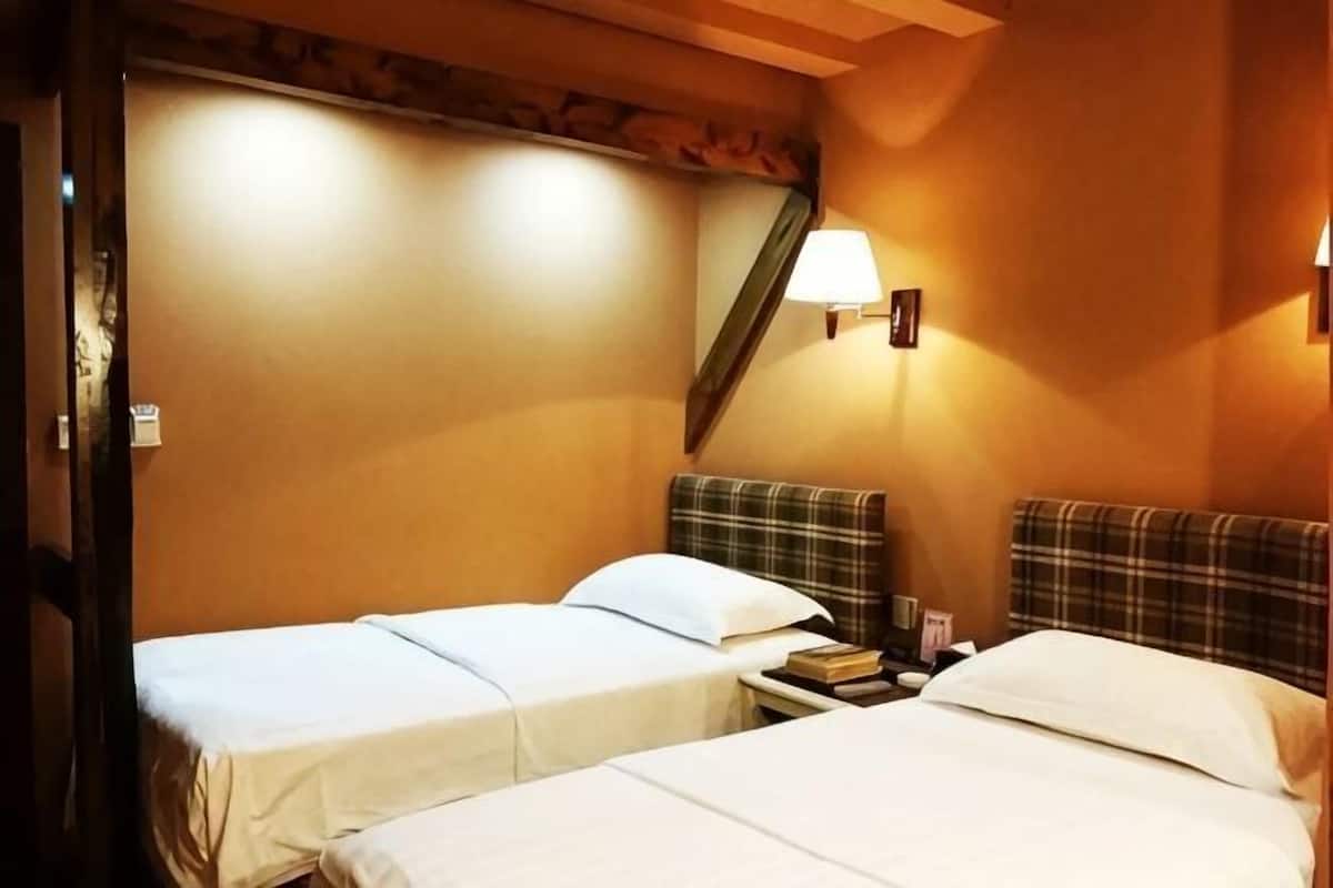 A hotel room with two beds, a nightstand with books, a lamp, and a mirror on the wall.