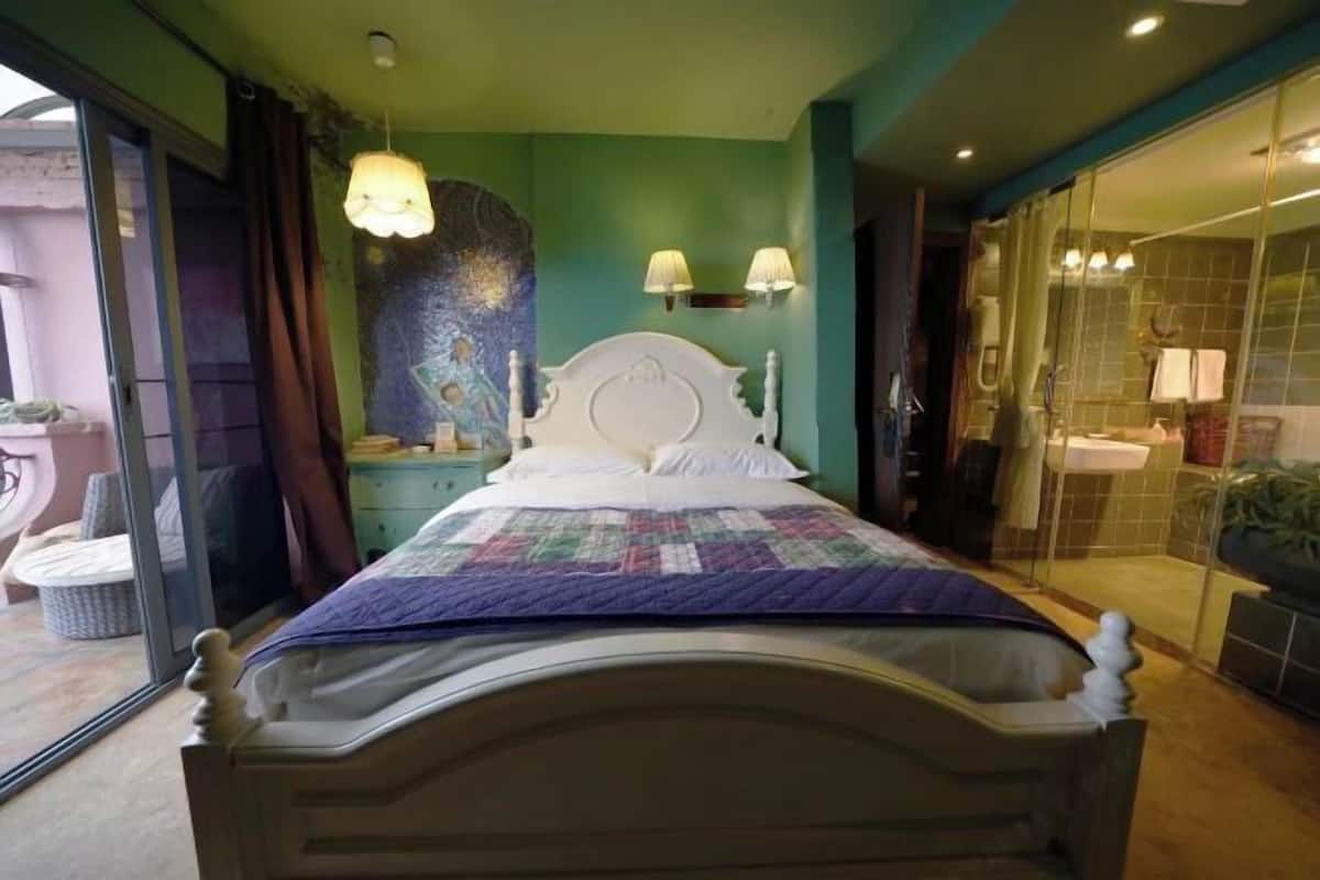 A bed with a white headboard, a colorful quilt, and two wall-mounted lamps.