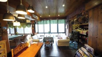 Un interior acogedor con techo de madera, zona de comedor con mesa y sillas, un sofá y una estantería.