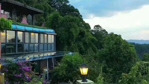 A modern building with a glass facade, surrounded by lush greenery and a mountainous backdrop. - Taole Forest Hostel (Chongqing)