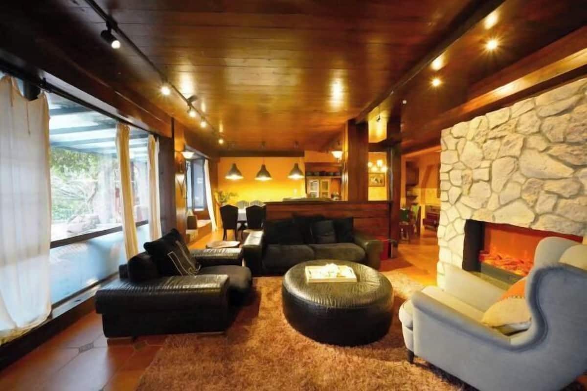 A cozy living room with a stone fireplace, leather sofas, and a large window overlooking a scenic view.