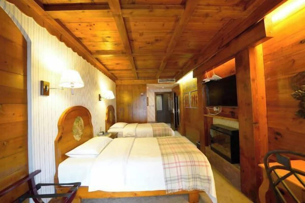A wooden cabin room with two beds, a television, and a fireplace.