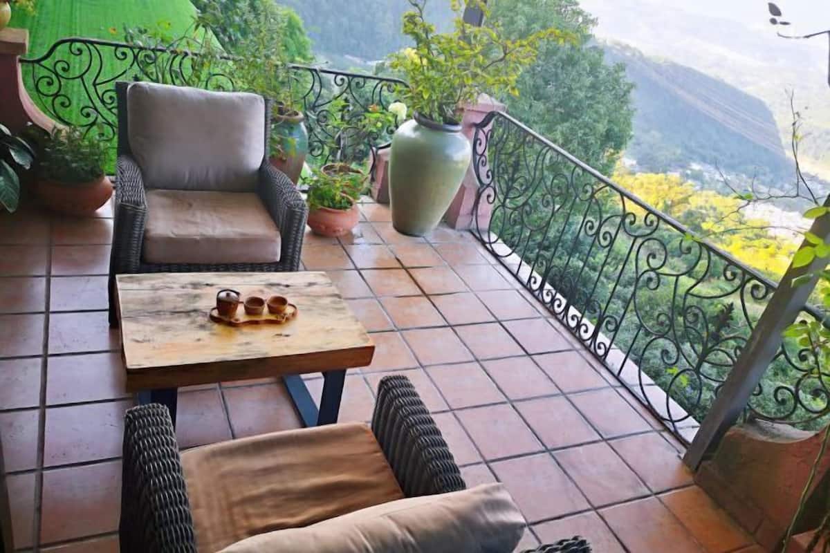 A balcony with wicker furniture, a tiled floor, and potted plants.