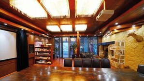 A spacious room with a large wooden table, leather seating, a stone wall, and a fireplace. - Taole Forest Hostel (Chongqing)
