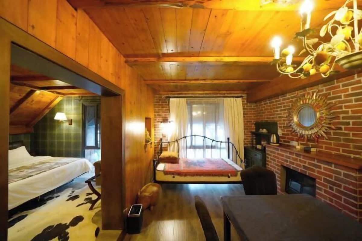 A cozy room with a bed, a bench, a fireplace, and a brick wall.