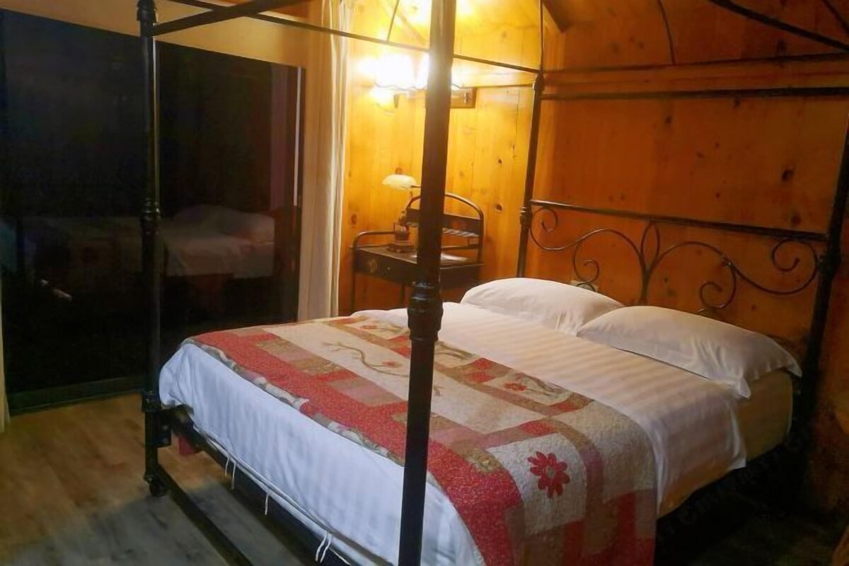 A four-poster bed with white linens and a floral-patterned bedspread in a wooden room with a wooden headboard.