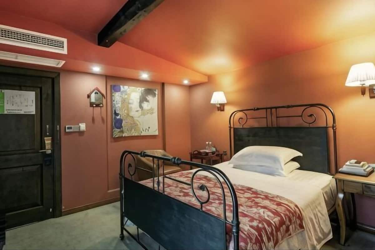 A room with a bed, a desk, a chair, a lamp, and a wall-mounted heater.