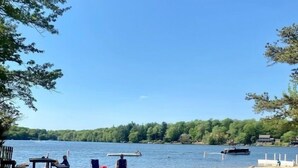 A sandy beach with a clear view of a lake, a dock, and a row of houses in the background.