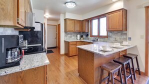 A modern kitchen with wooden cabinets, granite countertops, a central island with stools, and a built-in oven.