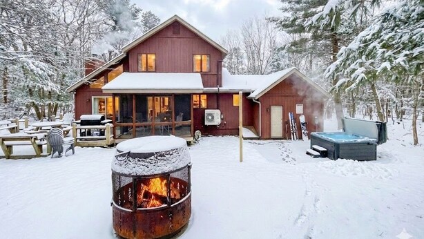 A lodge with a fire pit in the foreground, a hot tub, and a deck with outdoor seating.