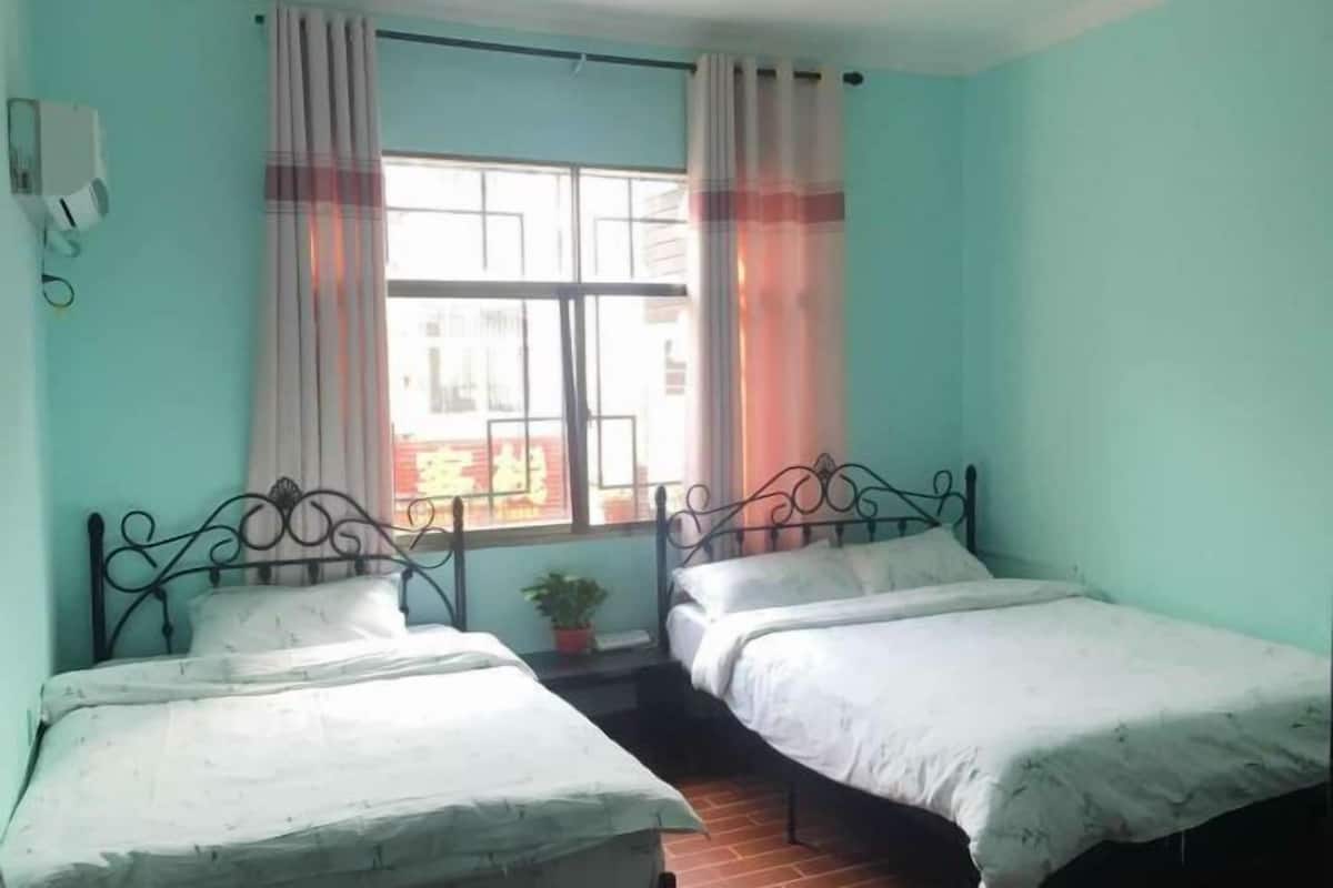Een kamer met twee eenpersoonsbedden, een raam met gordijnen, een bloempot en een wandairconditioning.