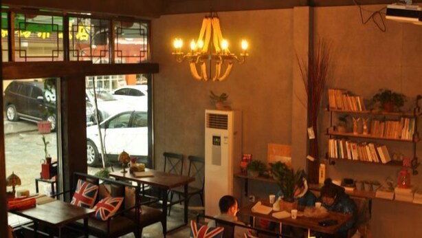 A cozy cafe with tables, chairs, a chandelier, and a bookshelf. - Huashijian Youth Hostel (Hengyang)
