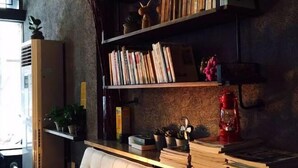 A cozy reading nook with a cushioned chair, a bookshelf filled with books, and a small table with decorative items. - Huashijian Youth Hostel (Hengyang)
