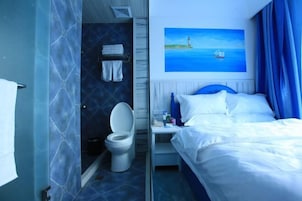 Una habitación de hotel con una cama, un cuadro de un faro, y un baño con inodoro y perchero para toallas.