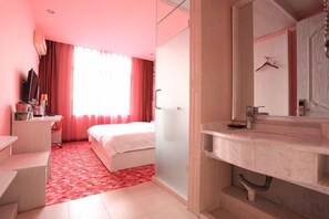 A hotel room with a bed, a desk, a mirror, and a bathroom with a sink. - Xintian'e Boutique Hotel (Ulanhot)