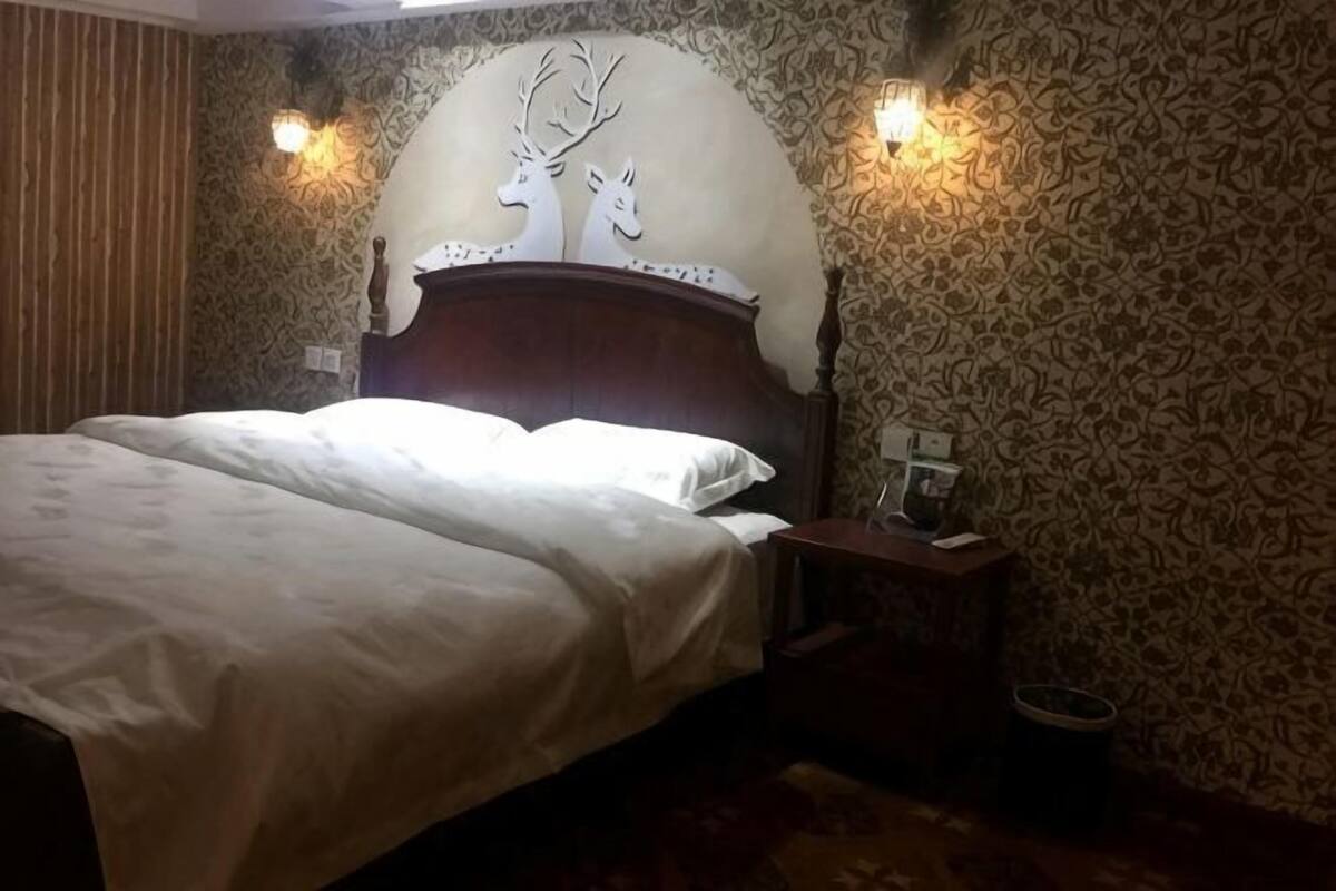 A bed with a headboard, two wall sconces, a nightstand, and patterned wallpaper.