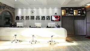 A hotel reception area with a modern design, featuring a reception desk, multiple computer monitors, a television, and a decorative wall with shelves. - Xintian'e Boutique Hotel (Ulanhot)