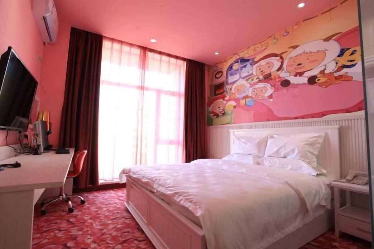 A bedroom with a bed, a desk, a chair, a television, and a wall with cartoon characters.