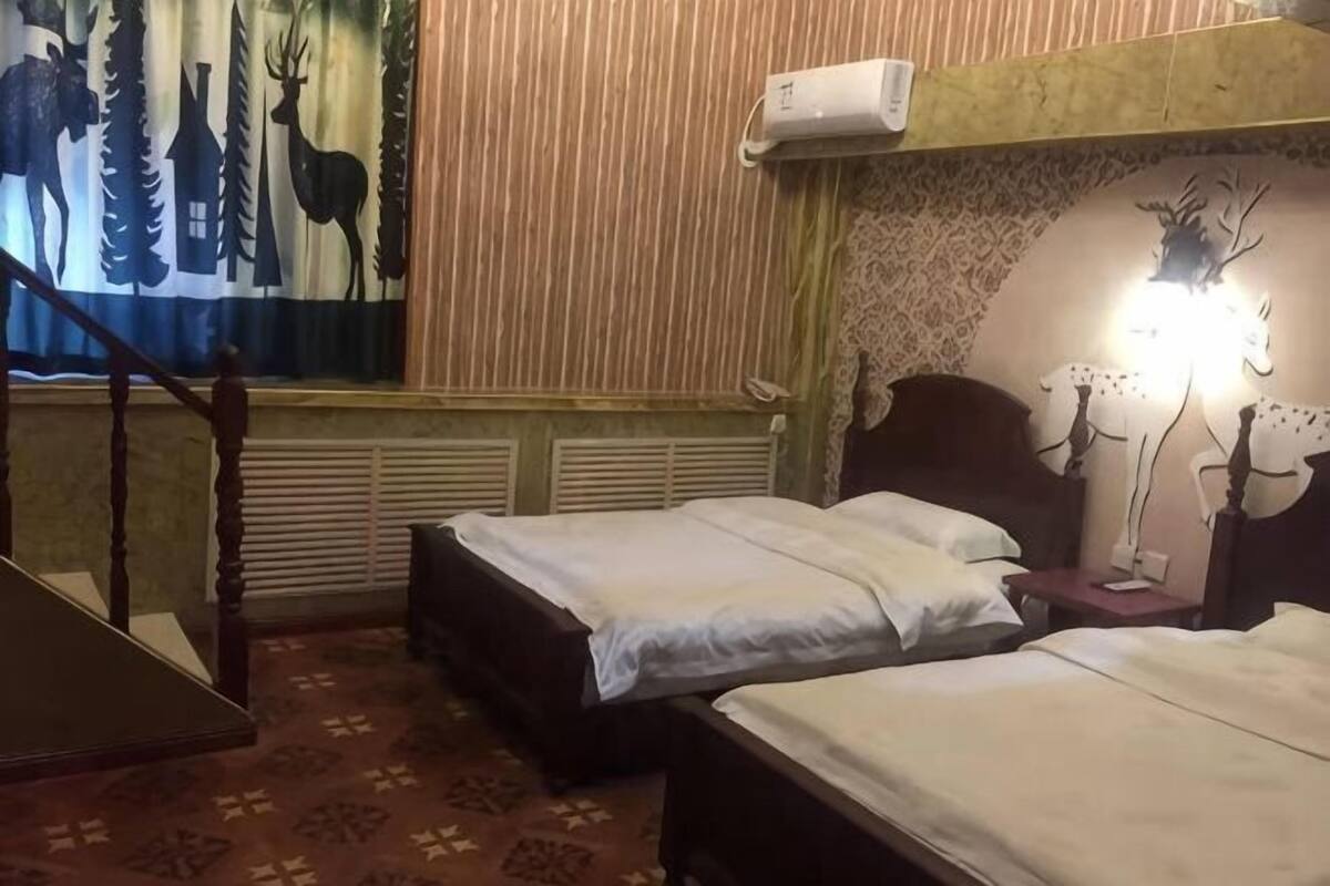 A room with two beds, a staircase, a patterned carpet, and a wall with a deer and tree mural.