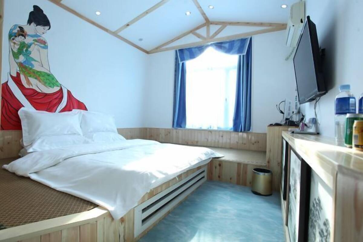 A room with a bed, a TV, a window with curtains, and a painting on the wall.