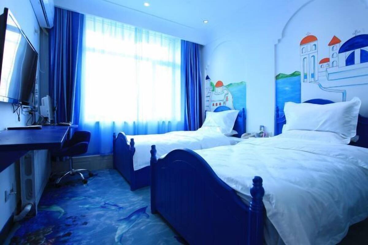 A hotel room with two beds, a desk, a chair, a TV, and a window with curtains.