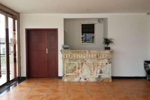 A room with a marble fireplace, a wooden door, and a potted plant. - Xintian'e Boutique Hotel (Ulanhot)