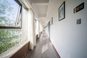 Un pasillo con piso de madera, ventanas grandes y un cartel con número en la pared.