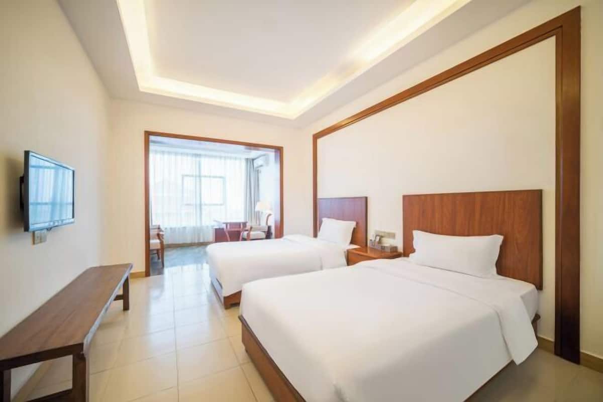 Une chambre d’hôtel avec deux lits, une télévision, un banc et un bureau.