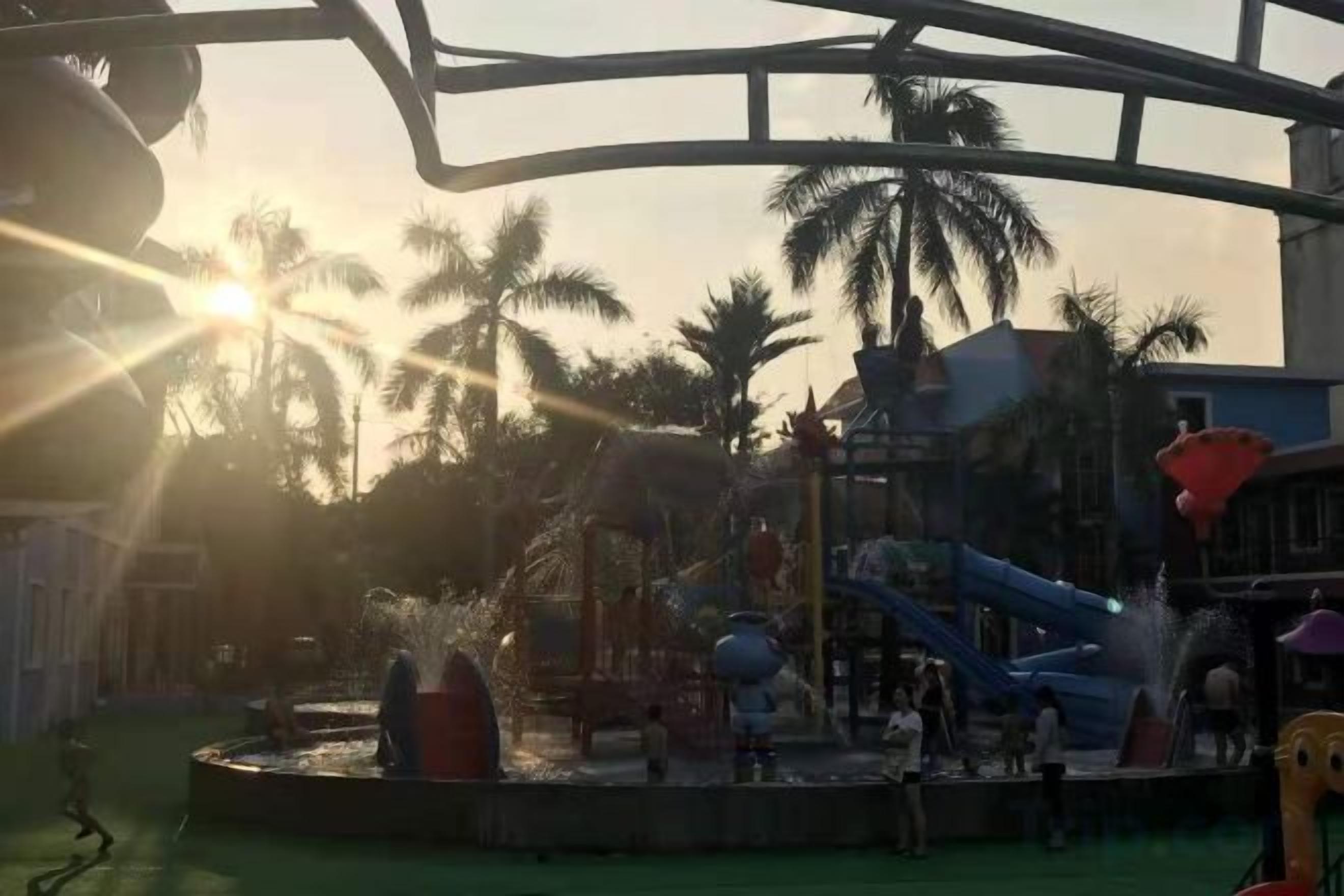 A water park with slides and fountains, surrounded by palm trees.