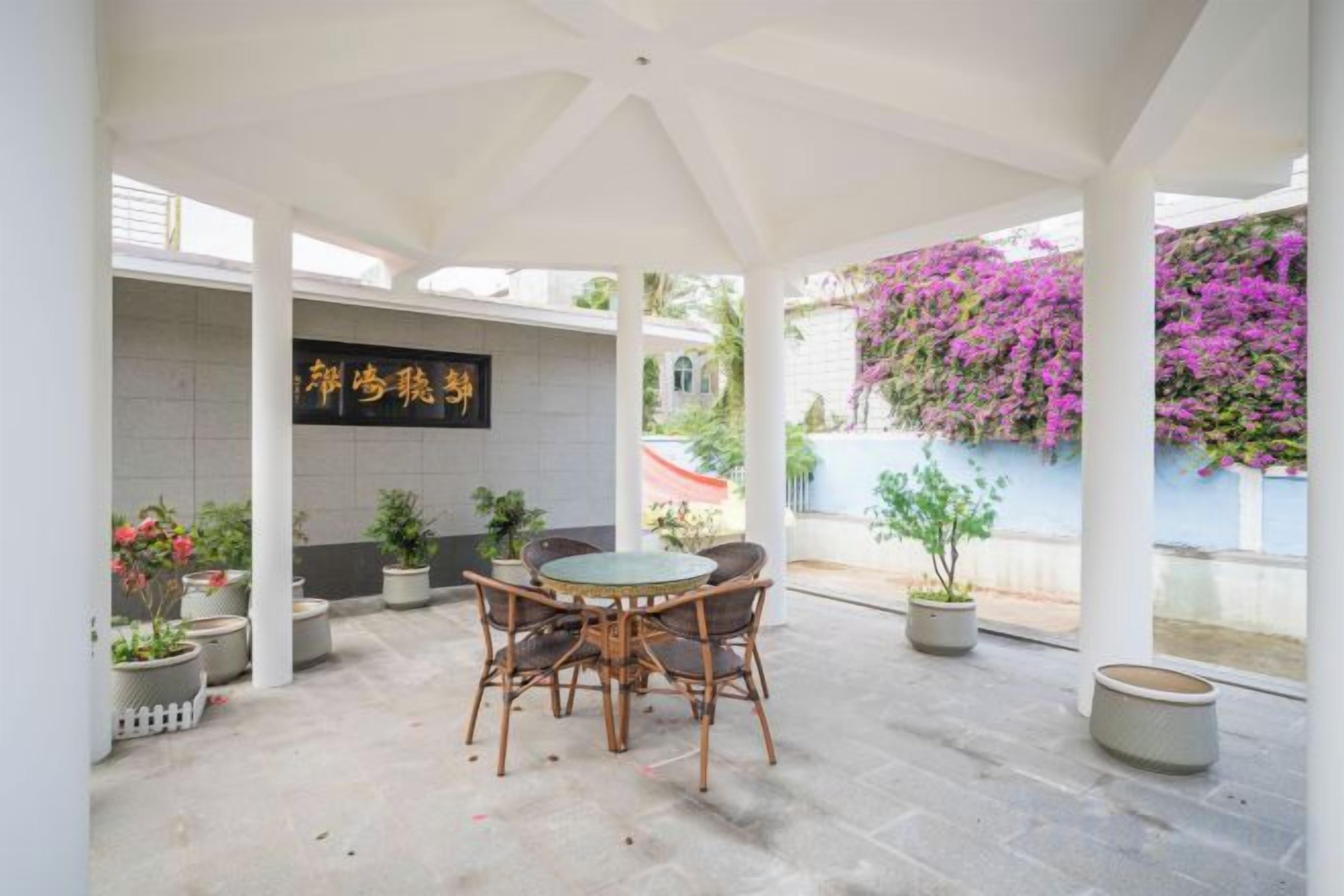 A covered patio area with a table and chairs, potted plants, and a wall with a sign.