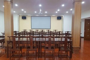 Una sala de conferencias con varias mesas y sillas, una pantalla de proyector y suelo de madera.