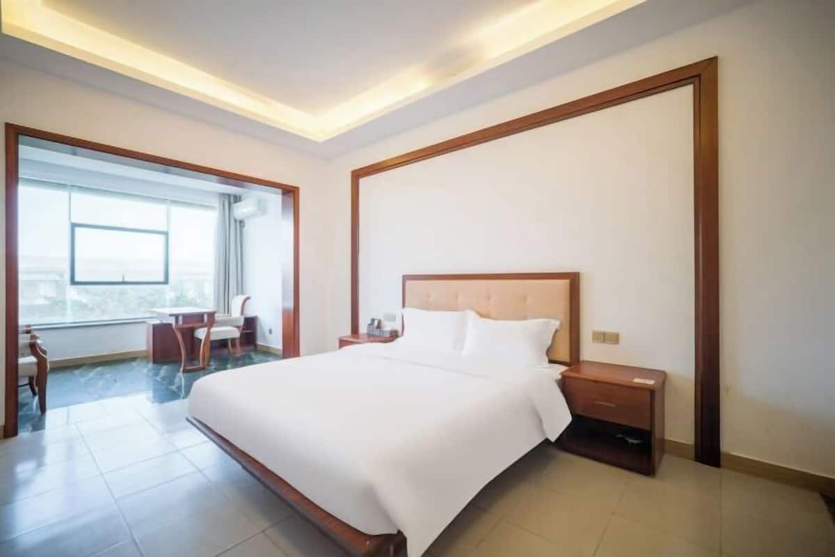 Une chambre d’hôtel avec un grand lit, un bureau et une chaise, une fenêtre donnant sur un beau paysage et une tête de lit en bois.
