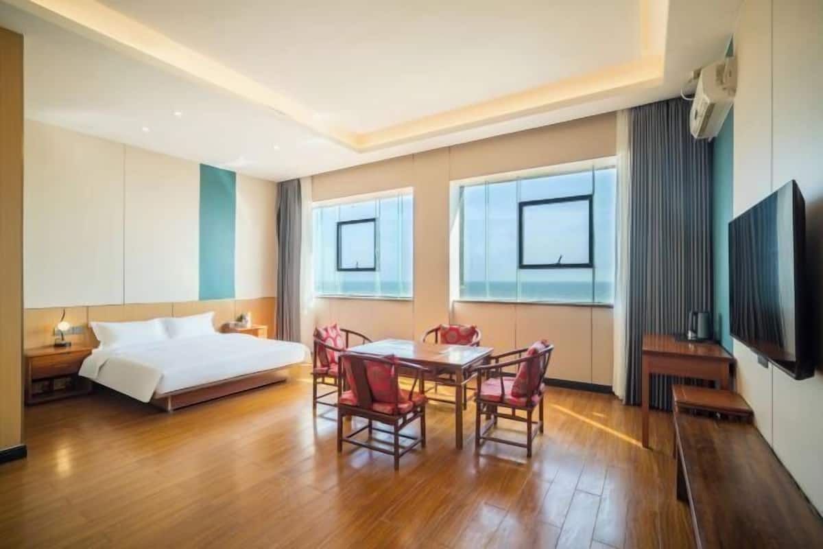 Une chambre d’hôtel avec un lit, une table à manger et des chaises, une télévision et de grandes fenêtres.