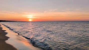 A sunset over a calm sea with a beach in the foreground.