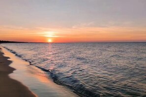 A sunset over a calm sea with a beach in the foreground.