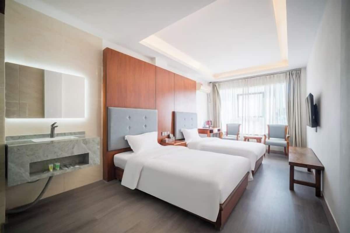 Une chambre d’hôtel avec deux lits, une salle de bain dotée d’un meuble-lavabo en marbre et un téléviseur fixé au mur.
