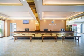 A reception area with a long counter, benches, and a wall-mounted television. - Xinsha Hotel (Zhanjiang)