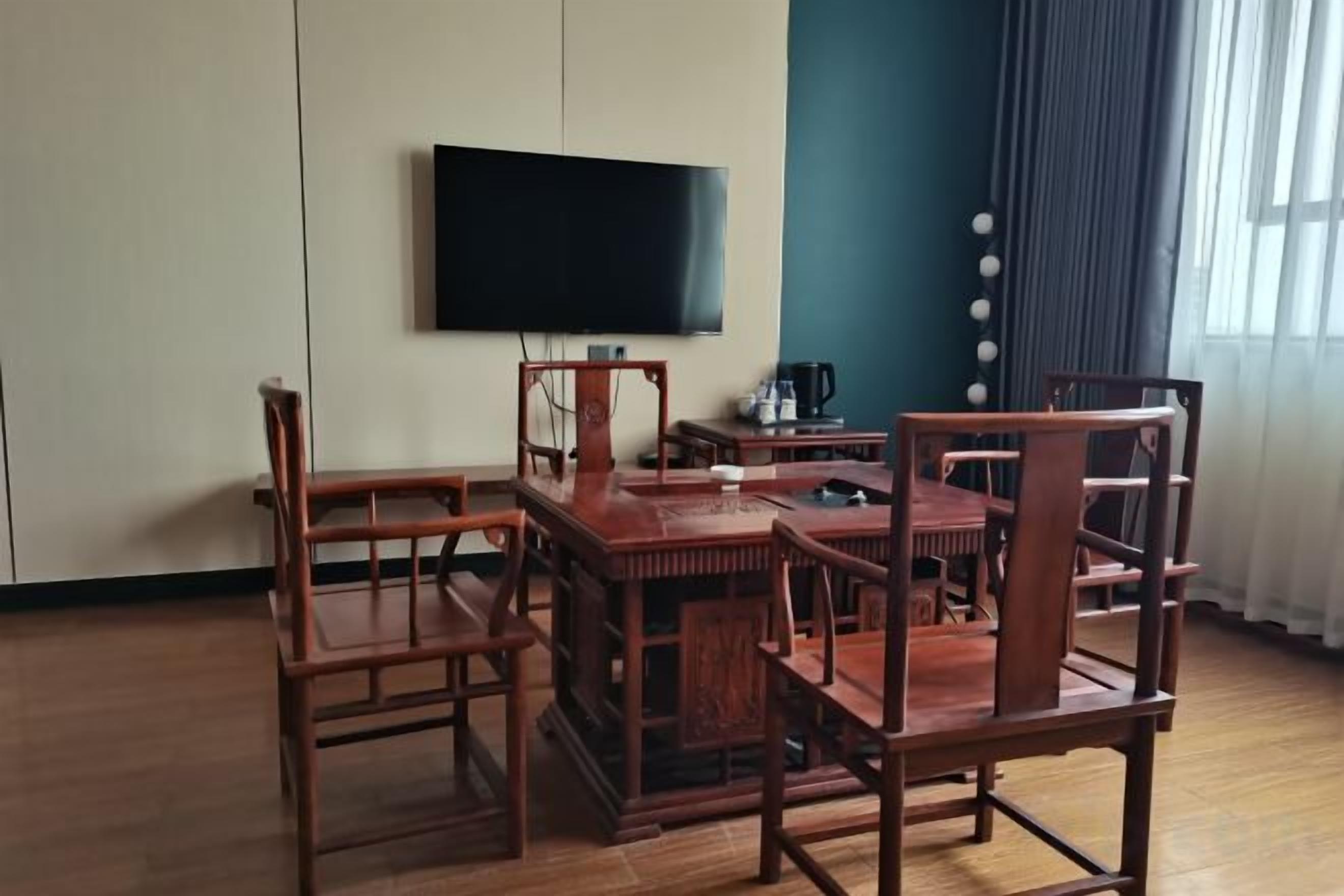 A room with a wooden dining table and chairs, a flat-screen TV mounted on the wall, and a window with curtains.
