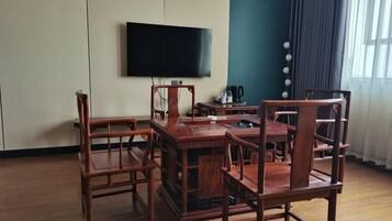 A room with a wooden dining table and chairs, a flat-screen TV mounted on the wall, and a window with curtains.