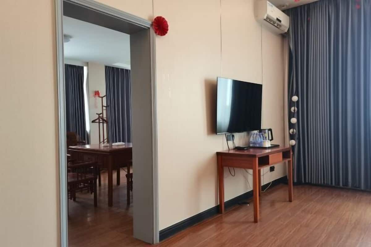 Une chambre d’hôtel avec un plancher en bois, un téléviseur posé sur un meuble, un bureau avec une bouilloire et une porte donnant sur une autre pièce.
