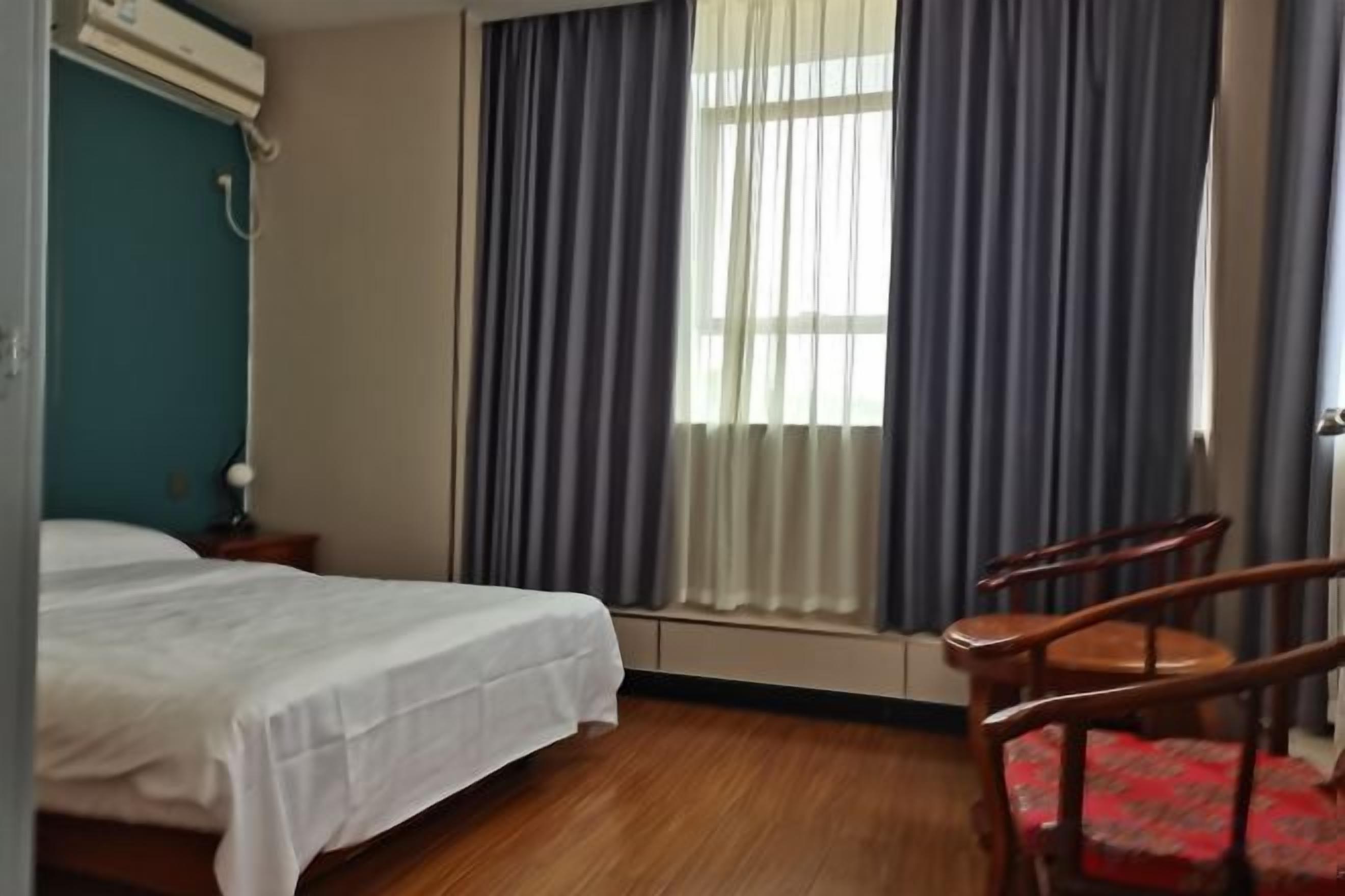 A hotel room with a bed, a chair, a window with curtains, and a radiator.